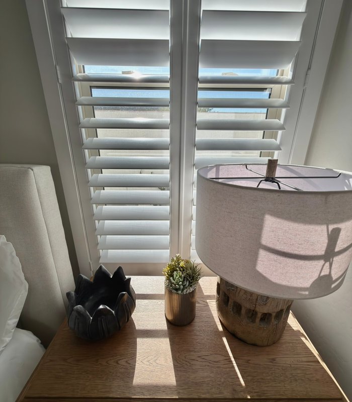 Nightstand beside a plantation-shuttered bedroom window casting louver shadows