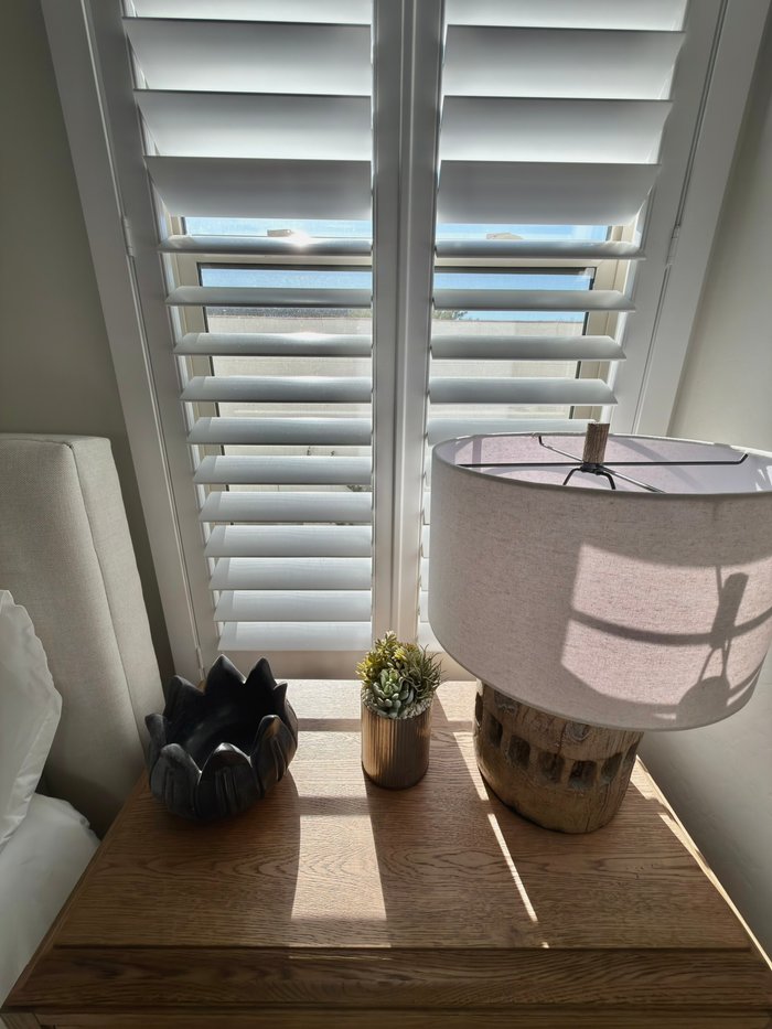 Louver shadows across a nightstand beside a shuttered bedroom window in a Gilbert, AZ home