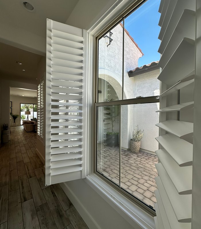 Large picture window with a shutter panel open onto a paved courtyard