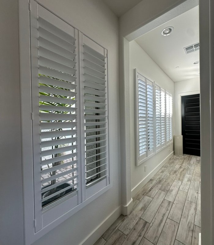 Hallway window shuttered in white with louvers open to garden greenery