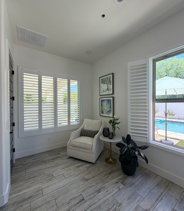 Bright sitting room with white plantation shutters on two window groups overlooking a backyard pool