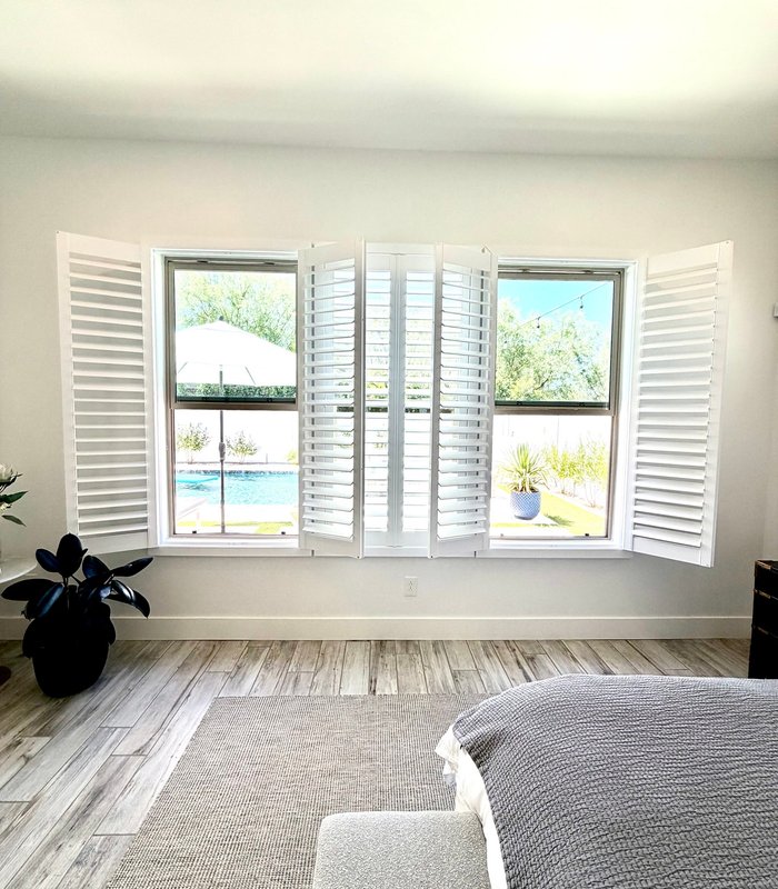 Bay window plantation shutters folded open across a bedroom wall