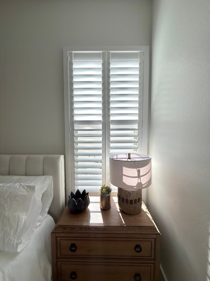 Full-height Norman shutters beside a bed in warm morning light, a Chandler, AZ bedroom install