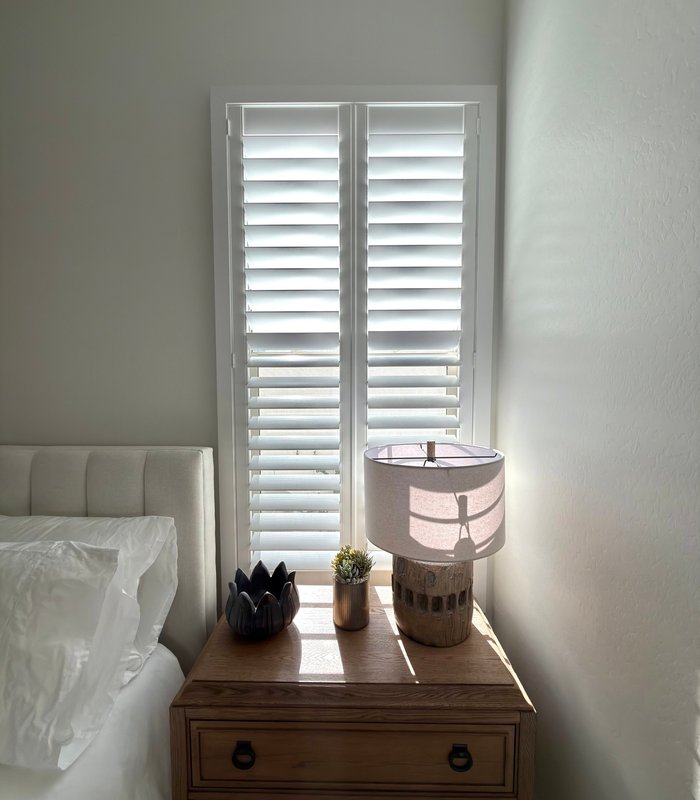 Bedside window with full-height Norman shutters and warm morning light