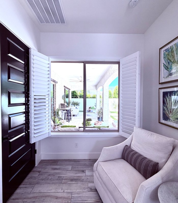 Sitting room window with Norman shutter panels folded back to open onto a covered patio and pool