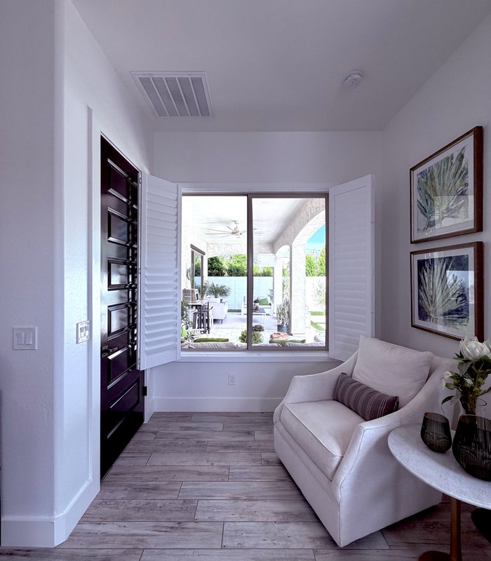Wide view of an entry sitting room, Norman shutters folded open across the window to the pool deck