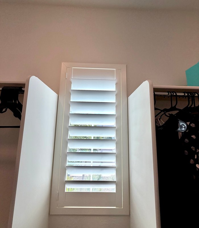 Narrow walk-in closet window fitted with a custom-measured Norman shutter, louvers tilted open