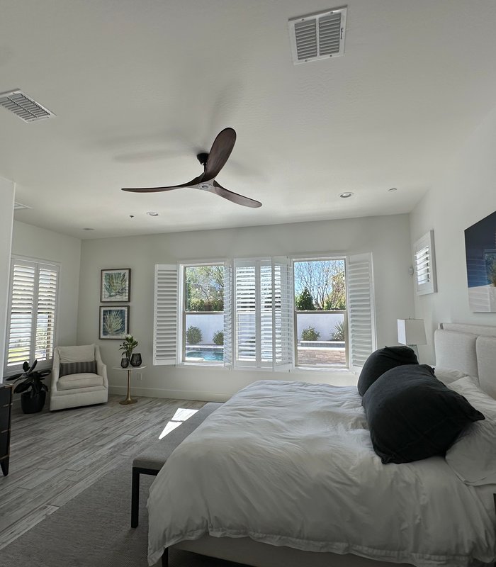 Wide view of a master bedroom with Norman shutters across the bay window and side windows
